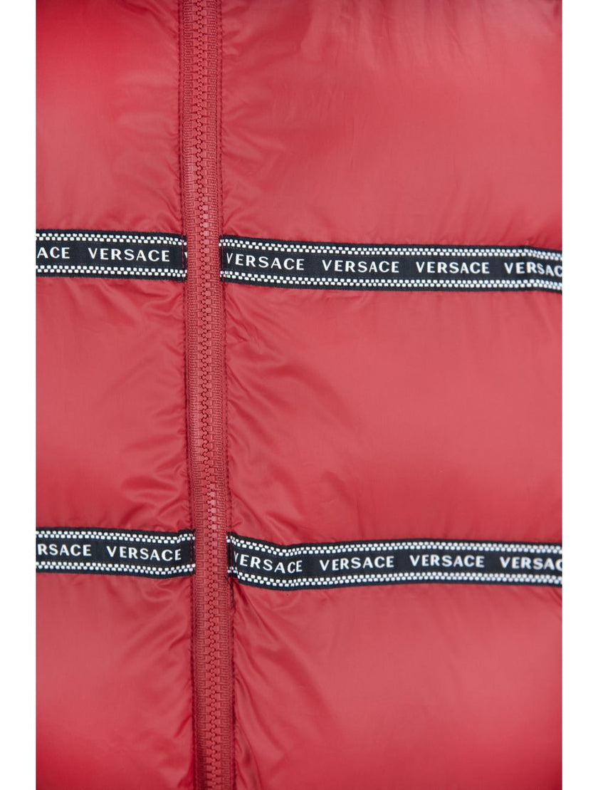 Elegant Red Versace Logo Vest with Detachable HoodDiscover opulence in outerwear with this stunning, brand new Versace vest. A harmonious blend of style and warmth, this piece boasts black bands adorned with the iconic white ‘Versace’ logo and a hood that