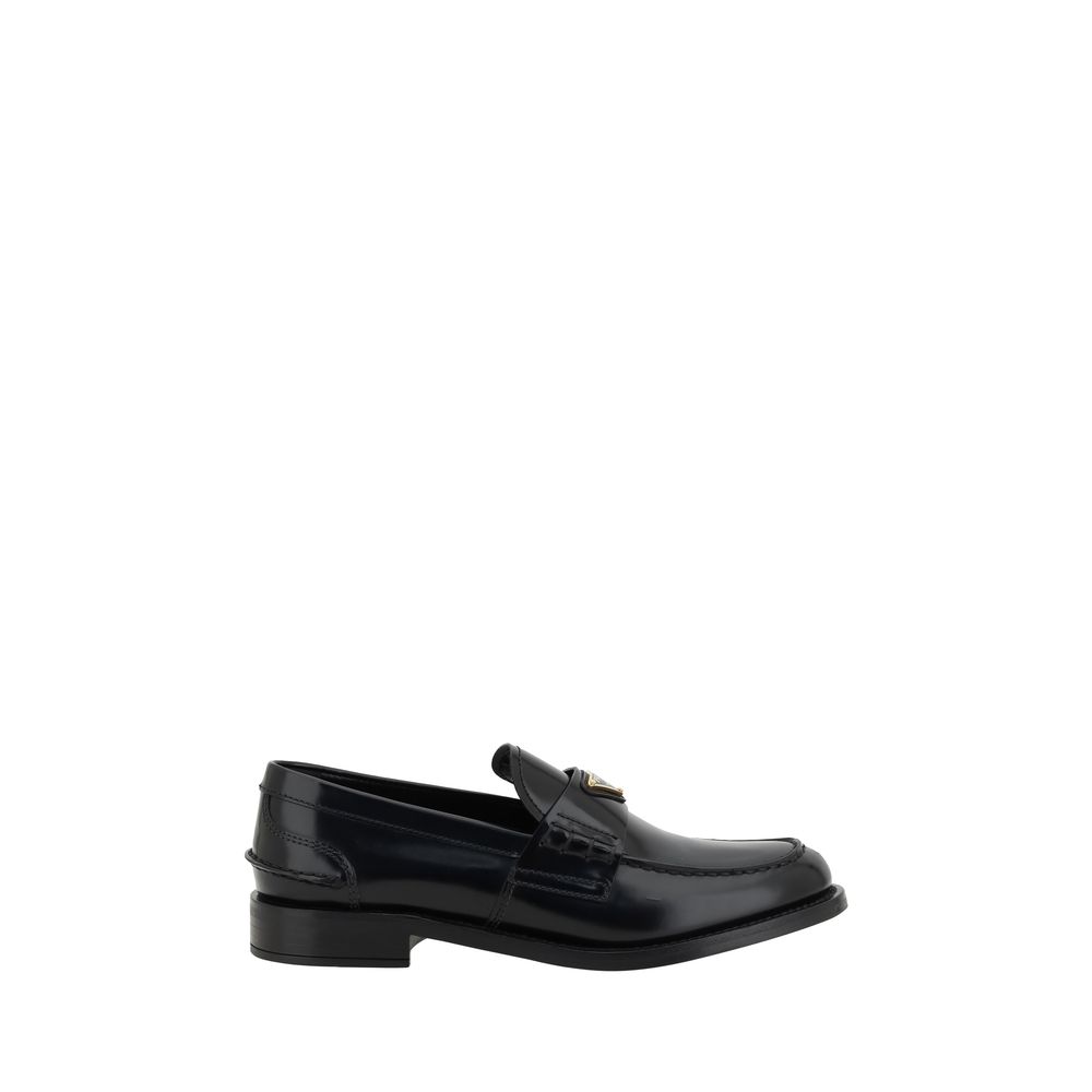 Black Leather Logo LoafersPrada’s Leather Loafers are a mix of classic elegance and distinctive details. The slightly elongated round toe and leather block heel ensure comfort and style. The iconic enameled triangular plaque with the brand’s signature app