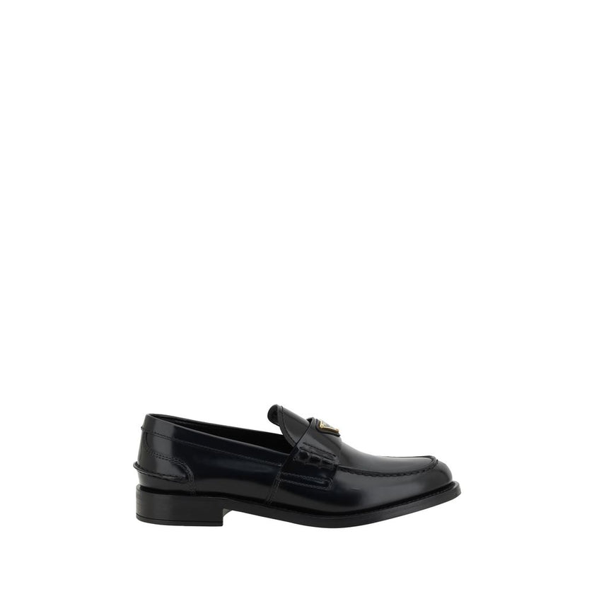 Black Leather Logo LoafersPrada’s Leather Loafers are a mix of classic elegance and distinctive details. The slightly elongated round toe and leather block heel ensure comfort and style. The iconic enameled triangular plaque with the brand’s signature app