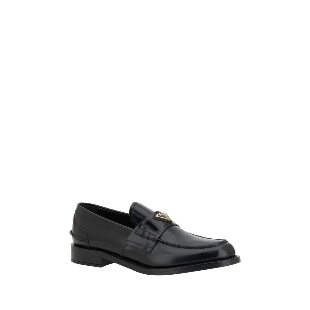Black Leather Logo LoafersPrada’s Leather Loafers are a mix of classic elegance and distinctive details. The slightly elongated round toe and leather block heel ensure comfort and style. The iconic enameled triangular plaque with the brand’s signature app
