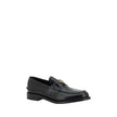 Black Leather Logo LoafersPrada’s Leather Loafers are a mix of classic elegance and distinctive details. The slightly elongated round toe and leather block heel ensure comfort and style. The iconic enameled triangular plaque with the brand’s signature app