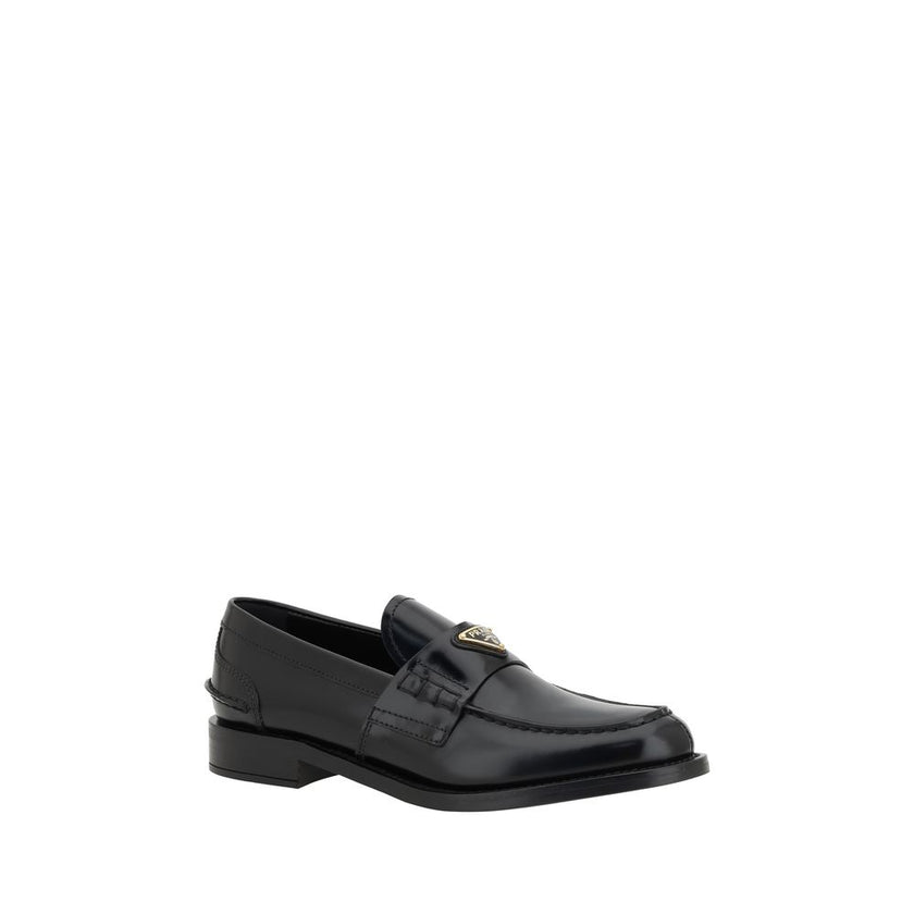 Black Leather Logo LoafersPrada’s Leather Loafers are a mix of classic elegance and distinctive details. The slightly elongated round toe and leather block heel ensure comfort and style. The iconic enameled triangular plaque with the brand’s signature app