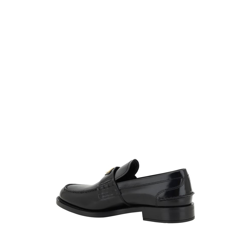 Black Leather Logo LoafersPrada’s Leather Loafers are a mix of classic elegance and distinctive details. The slightly elongated round toe and leather block heel ensure comfort and style. The iconic enameled triangular plaque with the brand’s signature app