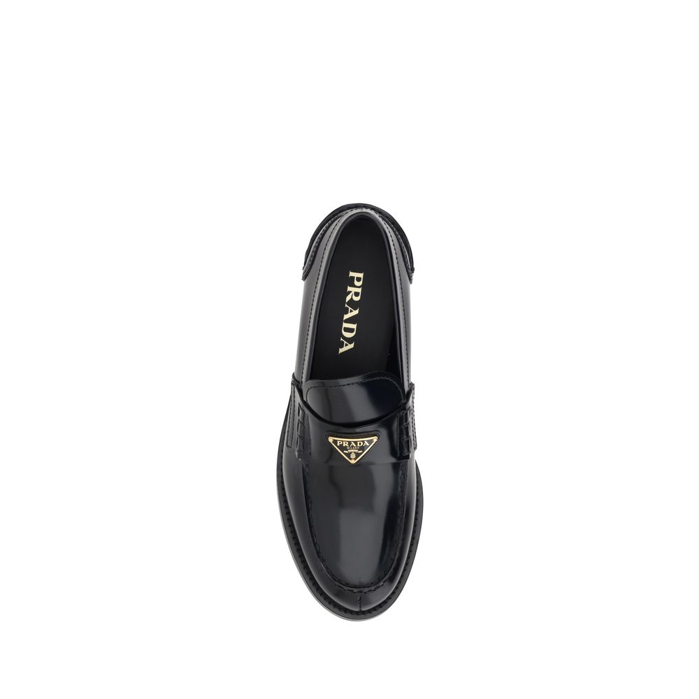 Black Leather Logo LoafersPrada’s Leather Loafers are a mix of classic elegance and distinctive details. The slightly elongated round toe and leather block heel ensure comfort and style. The iconic enameled triangular plaque with the brand’s signature app
