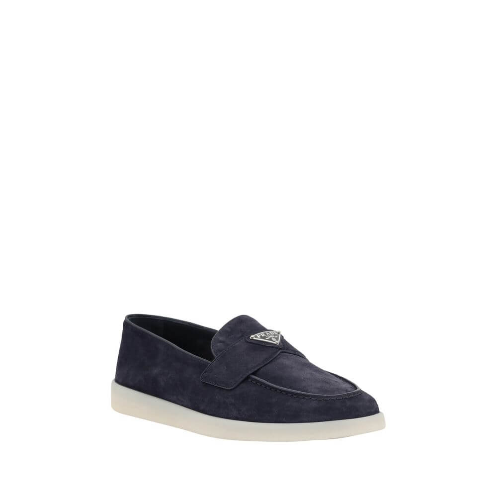 Blue Rubber Slip-On LoafersPrada’s leather Loafers feature an almond toe and a suede design that lends a touch of sophisticated elegance. The contrasting flat sole and front tray embellished with the brand’s iconic triangular plaque add a distinctive deta
