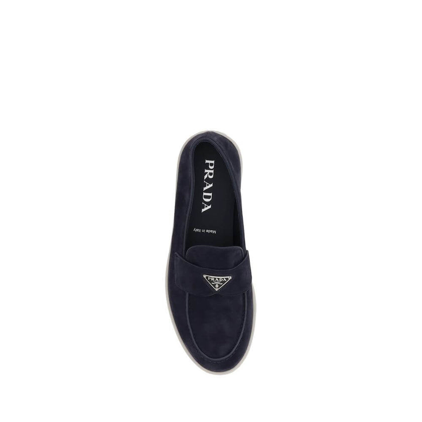 Blue Rubber Slip-On LoafersPrada’s leather Loafers feature an almond toe and a suede design that lends a touch of sophisticated elegance. The contrasting flat sole and front tray embellished with the brand’s iconic triangular plaque add a distinctive deta
