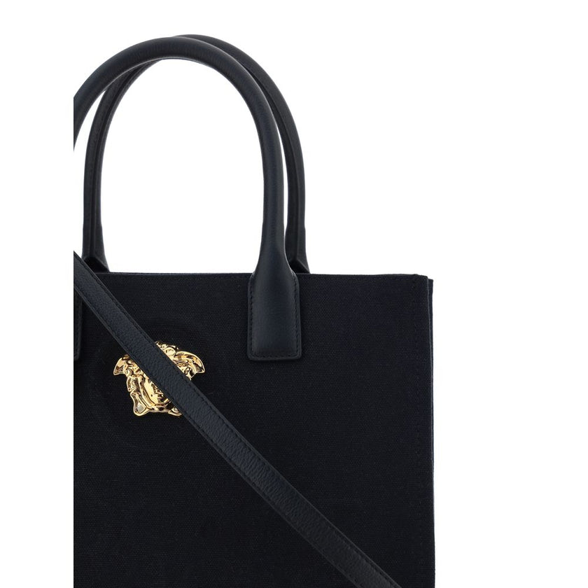 Black Cotton Shoulder BagCotton Shoulder Bag by Versace, rigid leather top handles, removable flat shoulder strap, top button closure, single interior compartment, iconic brand monogram embossed on front, leather feet at base, iconic Medusa embossed appli