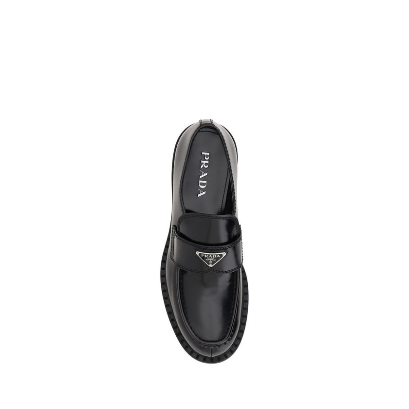 Black Rubber Platform LoafersPrada’s Leather Loafers revisit a classic with a bold, contemporary attitude. Featuring a slightly elongated round toe and a textured platform sole, they are distinguished by the iconic enameled triangular logo plaque applied