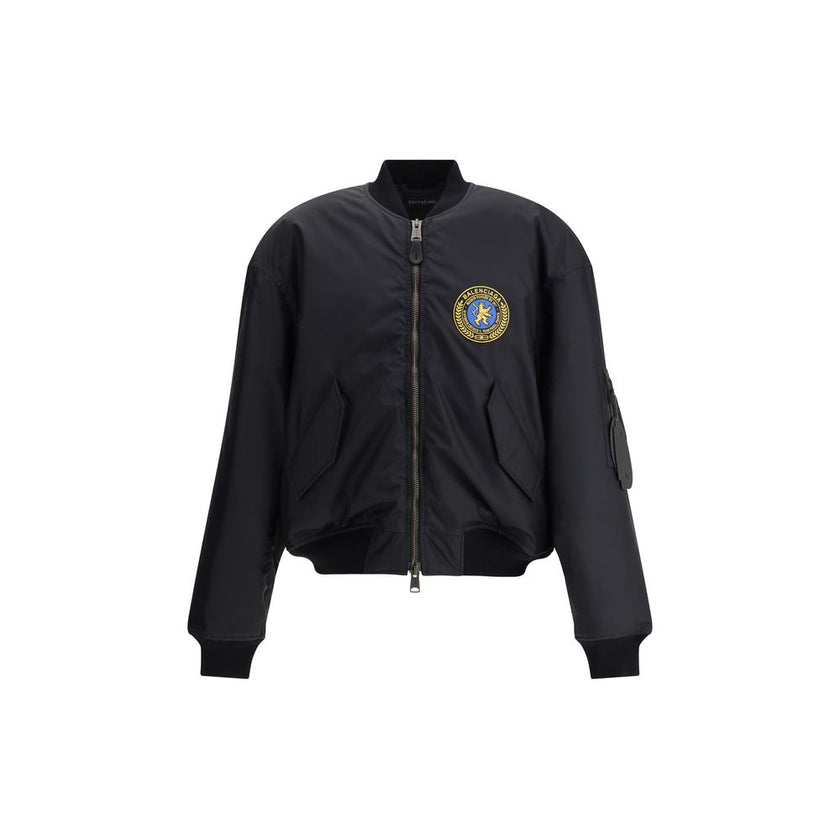 Black Polyamide BomberBalenciaga’s bomber Jacket features a zipper and pull tab closure, complemented by two flap pockets with snap buttons at the front. Ribbed edges define the garment’s profile, while a uniform chest applique adds a distinctive detail t