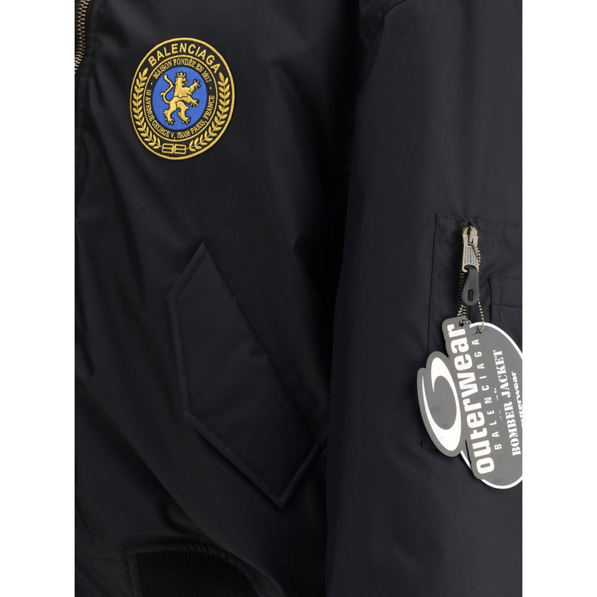 Black Polyamide BomberBalenciaga’s bomber Jacket features a zipper and pull tab closure, complemented by two flap pockets with snap buttons at the front. Ribbed edges define the garment’s profile, while a uniform chest applique adds a distinctive detail t