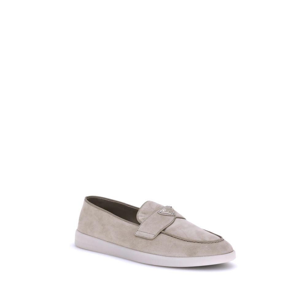Beige Rubber Slip-On LoafersPrada’s leather Loafers feature an almond toe and a suede design that lends a touch of sophisticated elegance. The contrasting flat sole and front tray embellished with the brand’s iconic triangular plaque add a distinctive det