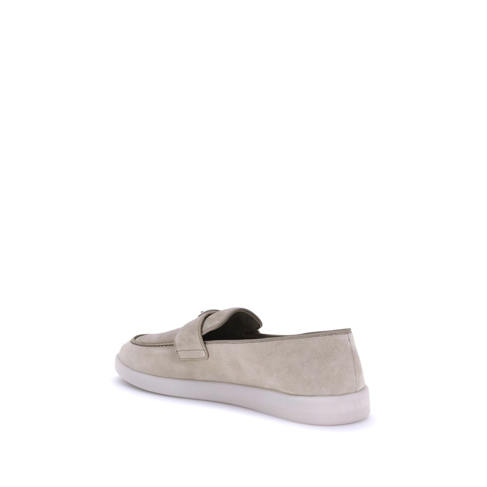 Beige Rubber Slip-On LoafersPrada’s leather Loafers feature an almond toe and a suede design that lends a touch of sophisticated elegance. The contrasting flat sole and front tray embellished with the brand’s iconic triangular plaque add a distinctive det