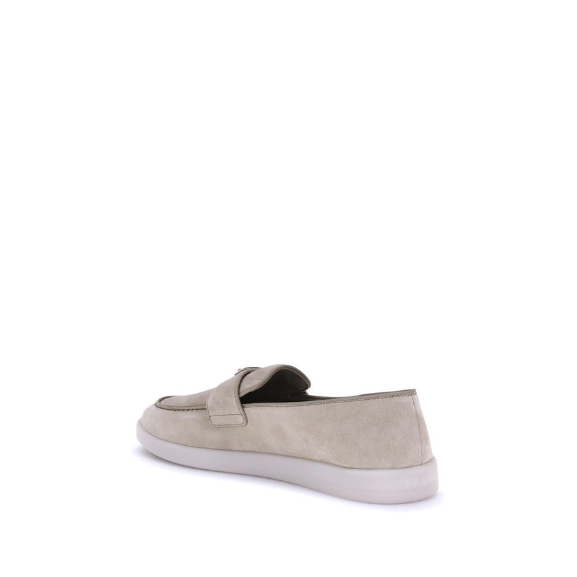 Beige Rubber Slip-On LoafersPrada’s leather Loafers feature an almond toe and a suede design that lends a touch of sophisticated elegance. The contrasting flat sole and front tray embellished with the brand’s iconic triangular plaque add a distinctive det