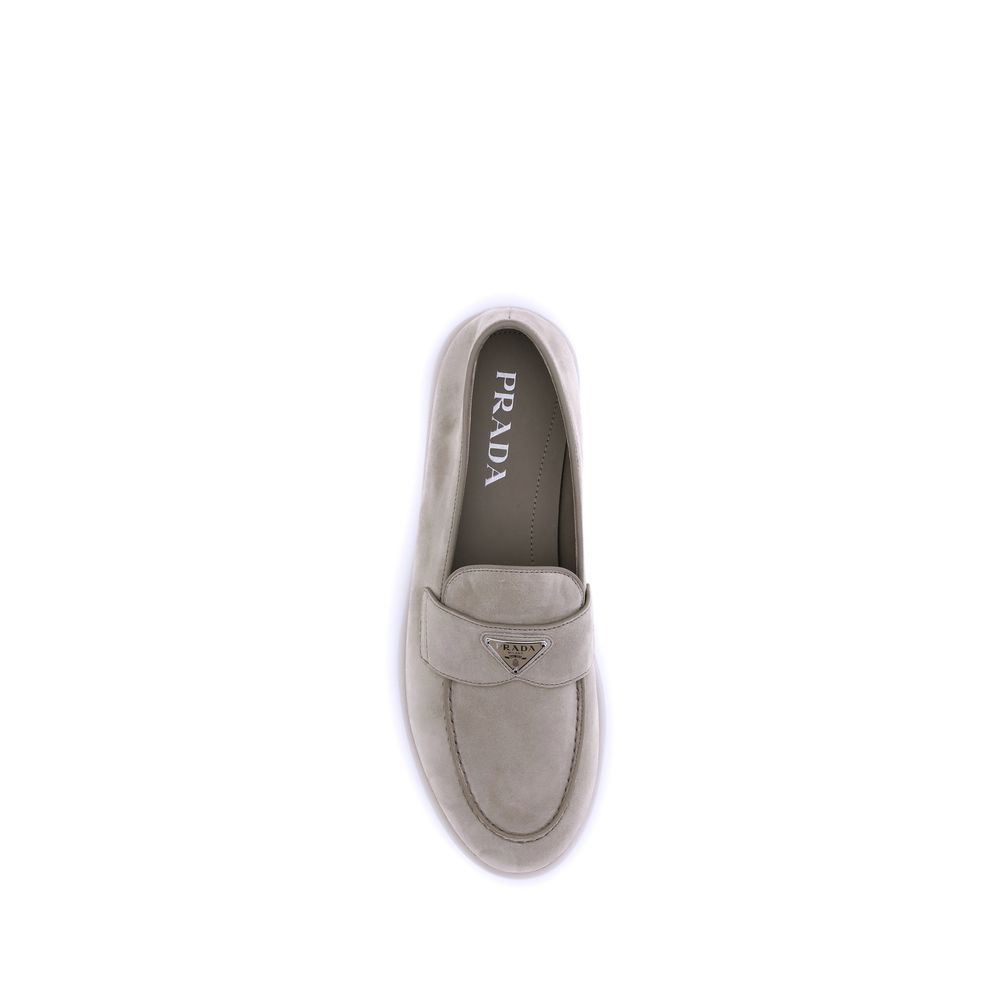 Beige Rubber Slip-On LoafersPrada’s leather Loafers feature an almond toe and a suede design that lends a touch of sophisticated elegance. The contrasting flat sole and front tray embellished with the brand’s iconic triangular plaque add a distinctive det