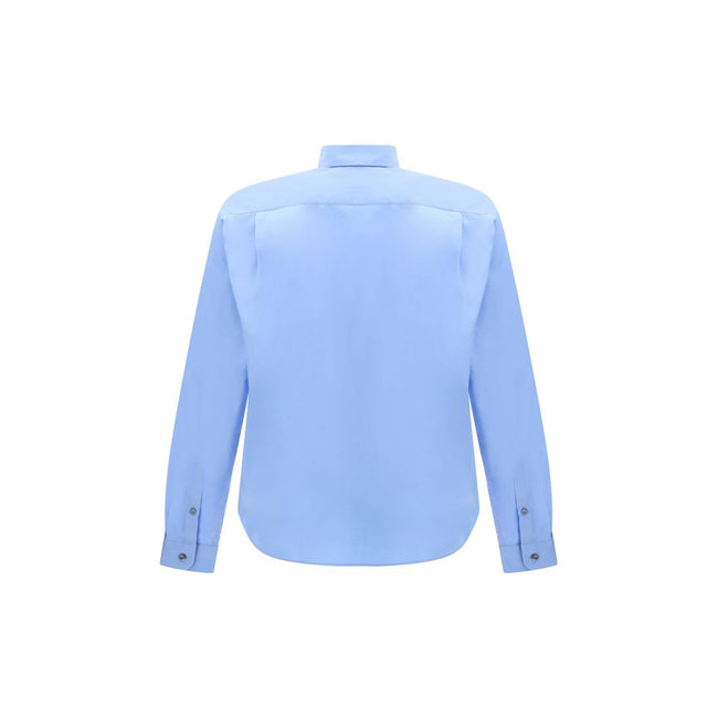 Light Blue Cotton Dress ShirtThe Prada Cotton Shirt is an essential piece with a refined style. Featuring a classic collar and front button closure, it stands out for the iconic signature sewn on the front, a discreet but unmistakable detail. Season: AW25