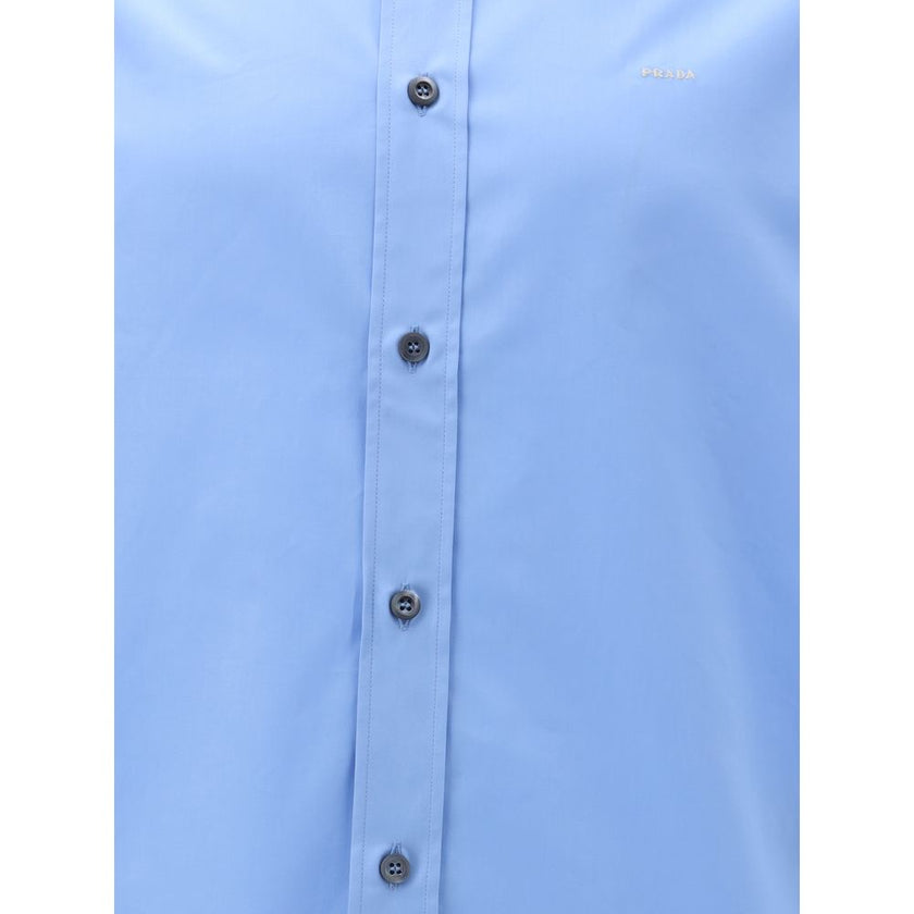 Light Blue Cotton Dress ShirtThe Prada Cotton Shirt is an essential piece with a refined style. Featuring a classic collar and front button closure, it stands out for the iconic signature sewn on the front, a discreet but unmistakable detail. Season: AW25