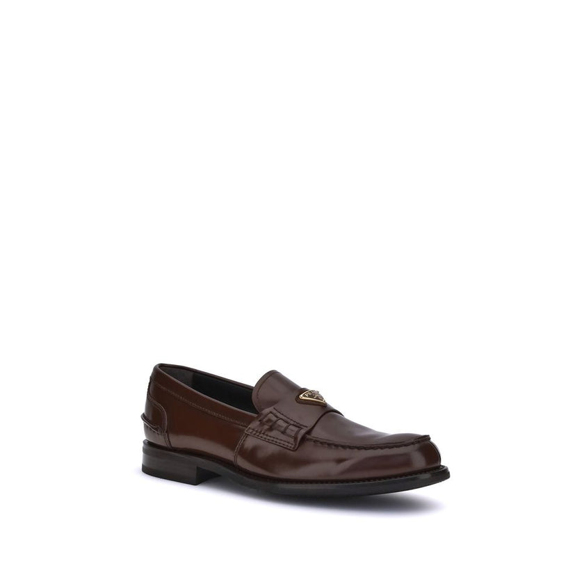Brown Calf Leather Bos Taurus Slip-On LoafersPrada’s leather Loafers are a mix of classic elegance and distinctive details. The slightly elongated round toe and leather block heel ensure comfort and style. The iconic enameled triangular plaque with the br