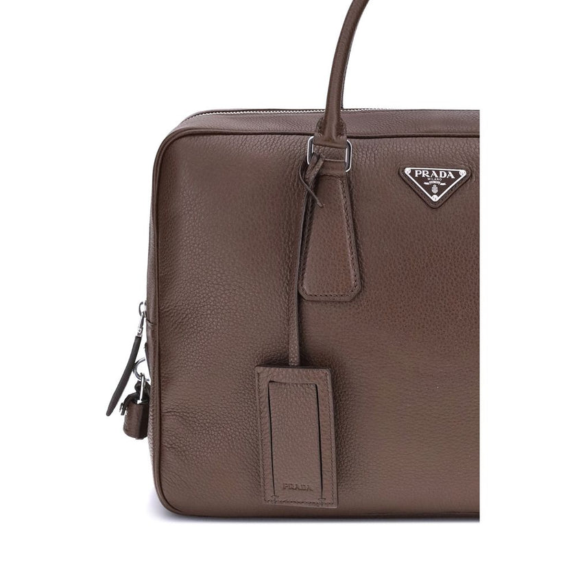 Brown Calf Leather Bos Taurus BriefcasePrada’s Men’s Handbag is an elegant and functional accessory designed to accompany everyday life in style. Equipped with two round handles and a top zipper closure, it features the iconic triangular plaque applied on