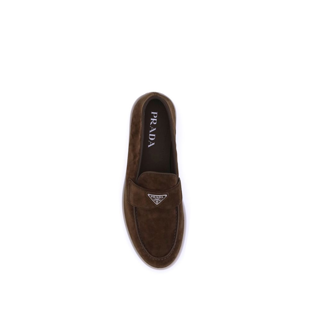 Brown Rubber Slip-On LoafersPrada’s leather Loafers feature an almond toe and a suede design that lends a touch of sophisticated elegance. The contrasting flat sole and front tray embellished with the brand’s iconic triangular plaque add a distinctive det