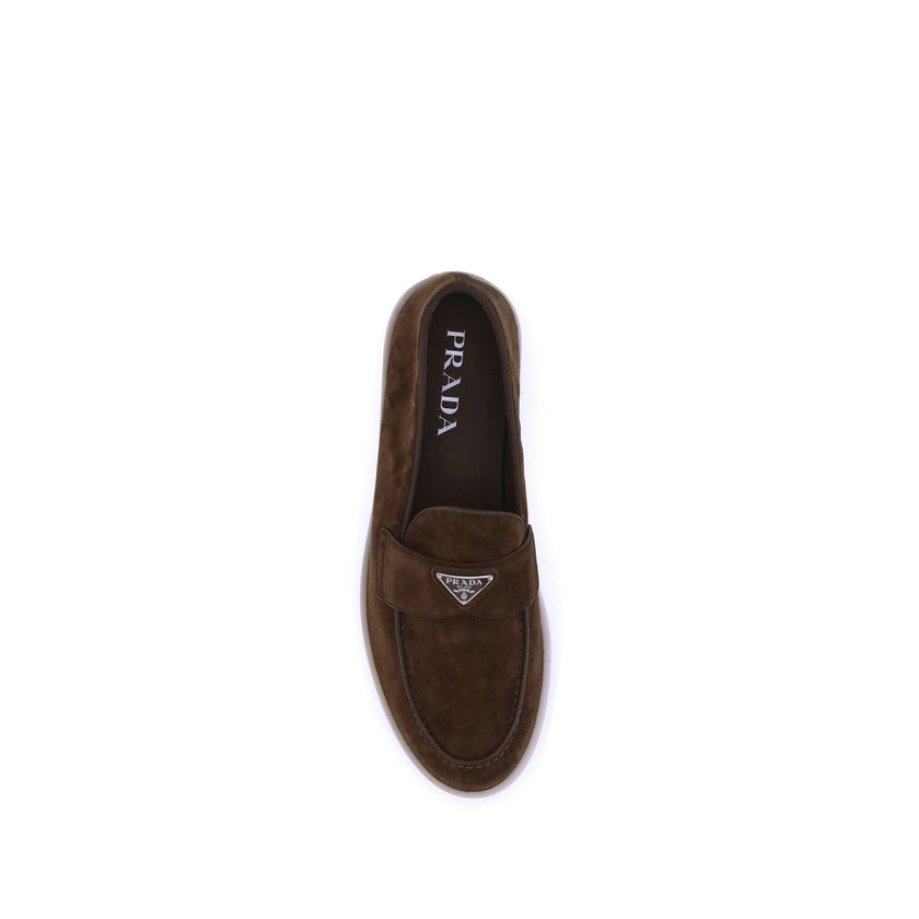 Brown Rubber Slip-On LoafersPrada’s leather Loafers feature an almond toe and a suede design that lends a touch of sophisticated elegance. The contrasting flat sole and front tray embellished with the brand’s iconic triangular plaque add a distinctive det