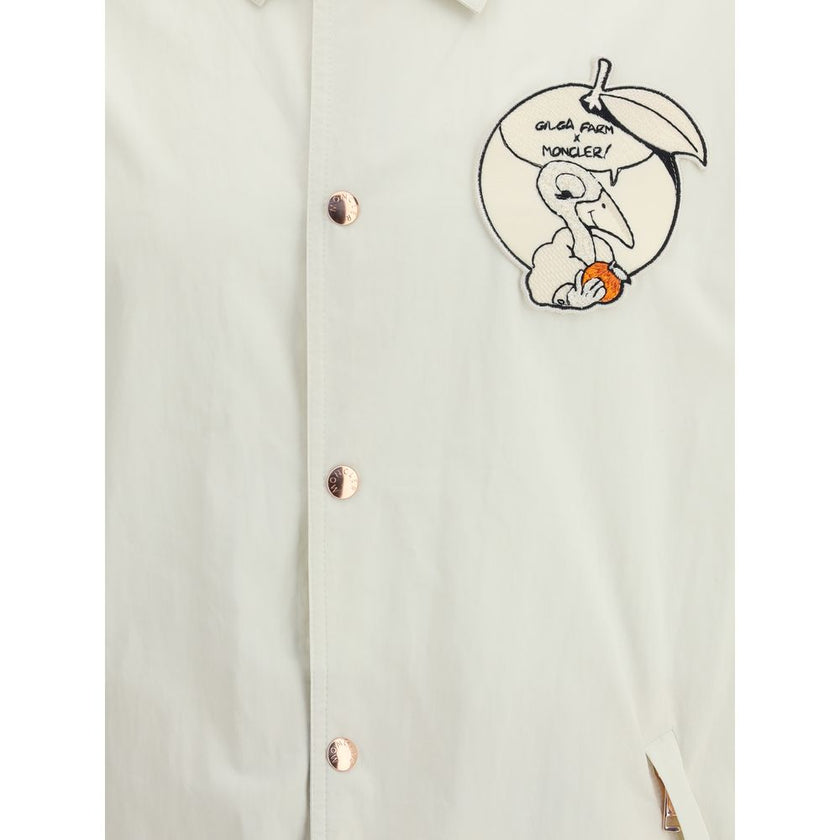 White Cotton CoatThe Moncler x Gilga Farm Satsuma Shirt Jacket by Donald Glover fuses workwear style and visual storytelling. Crafted from durable cotton and nylon canvas, it is part of the Moncler Genius line and stands out for its comic-style patches an
