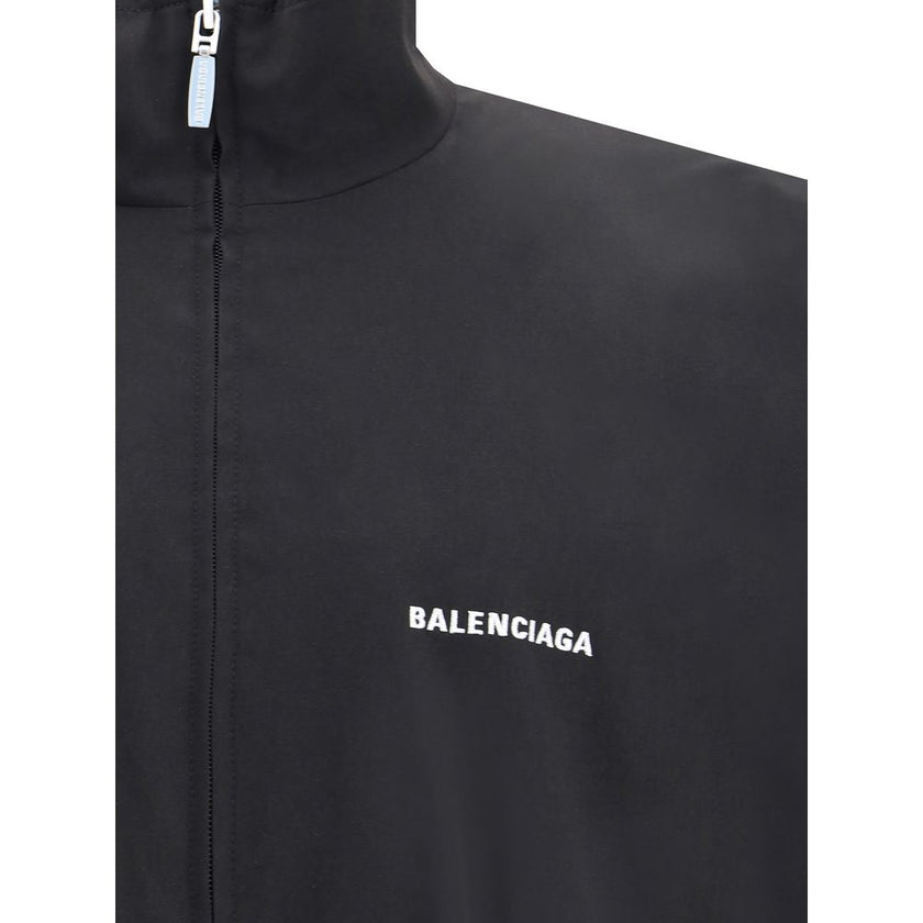 Black Polyester Shell JacketBalenciaga’s Oversized Windbreaker Jacket is a garment with a bold, sporty aesthetic made from durable technical fabric. Featuring contrasting Balenciaga embroidery on the chest and back, it has a high collar, concealed front z