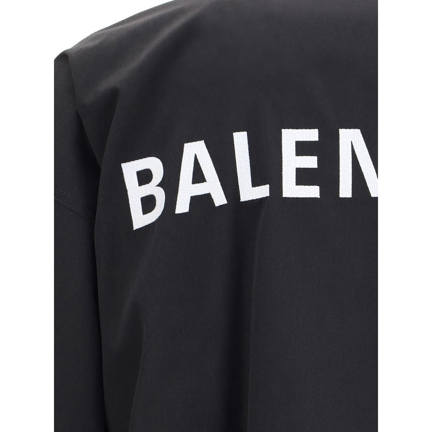 Black Polyester Shell JacketBalenciaga’s Oversized Windbreaker Jacket is a garment with a bold, sporty aesthetic made from durable technical fabric. Featuring contrasting Balenciaga embroidery on the chest and back, it has a high collar, concealed front z