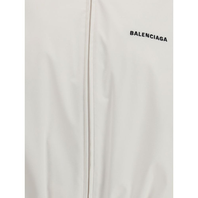 White Polyester Shell JacketBalenciaga’s Windbreaker Jacket is made of technical fabric and features contrasting logo embroidery on the chest and back. Featuring a high collar and concealed zipper closure, it offers two front zipper pockets. Gathered elas