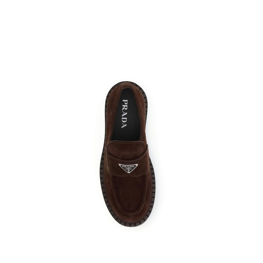 Brown Calf Leather Bos Taurus Slip-On LoafersPrada’s Suede Loafers combine classic elegance with iconic details. Characterized by the enameled metal triangle logo on the front, they feature a one-piece rubber sole with a branded logo, ensuring comfort and
