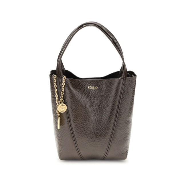 Spin Shoulder BagThe Spin Shoulder Bag by Chloé, crafted by shiny grained leather, features an elegant design with two flat top handles and an adjustable shoulder strap. The closure is secured by a magnetic button, while the detail of the hanging chain wi