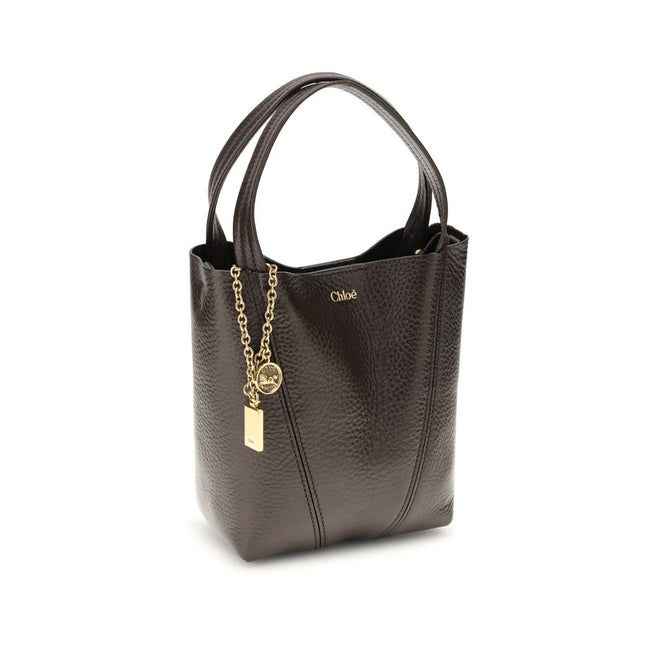 Spin Shoulder BagThe Spin Shoulder Bag by Chloé, crafted by shiny grained leather, features an elegant design with two flat top handles and an adjustable shoulder strap. The closure is secured by a magnetic button, while the detail of the hanging chain wi