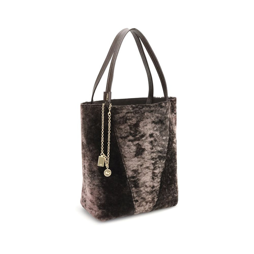 Brown Lamb Ovis Aries Aries Shoulder BagThe Spin Shearling Tote Bag by Chloé is a dark brown shearling tote accented with gold-tone hardware. It features double handles and a decorative chain with Chloé and Horse pendants. The tone-on-tone interior comple