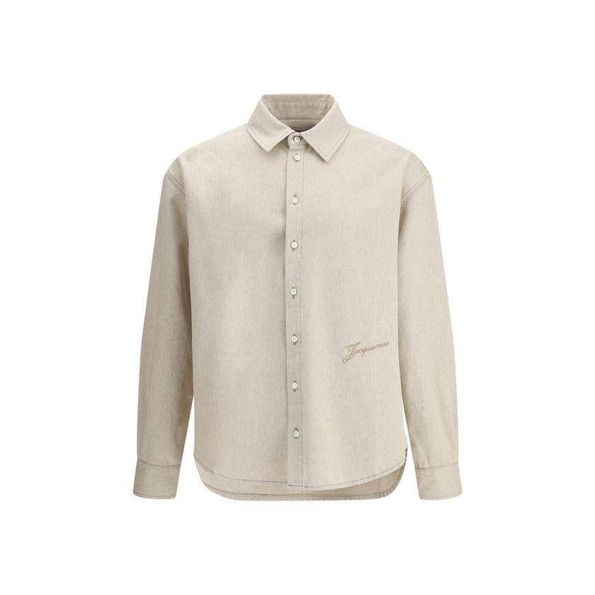 Beige Denim ShirtThe Simon denim Shirt in de-Nîmes by Jacquemus reinterprets a wardrobe classic with the Maison’s refined, contemporary spirit. Crafted from soft cotton and hemp denim, it features a straight fit that falls naturally along the body. A poin