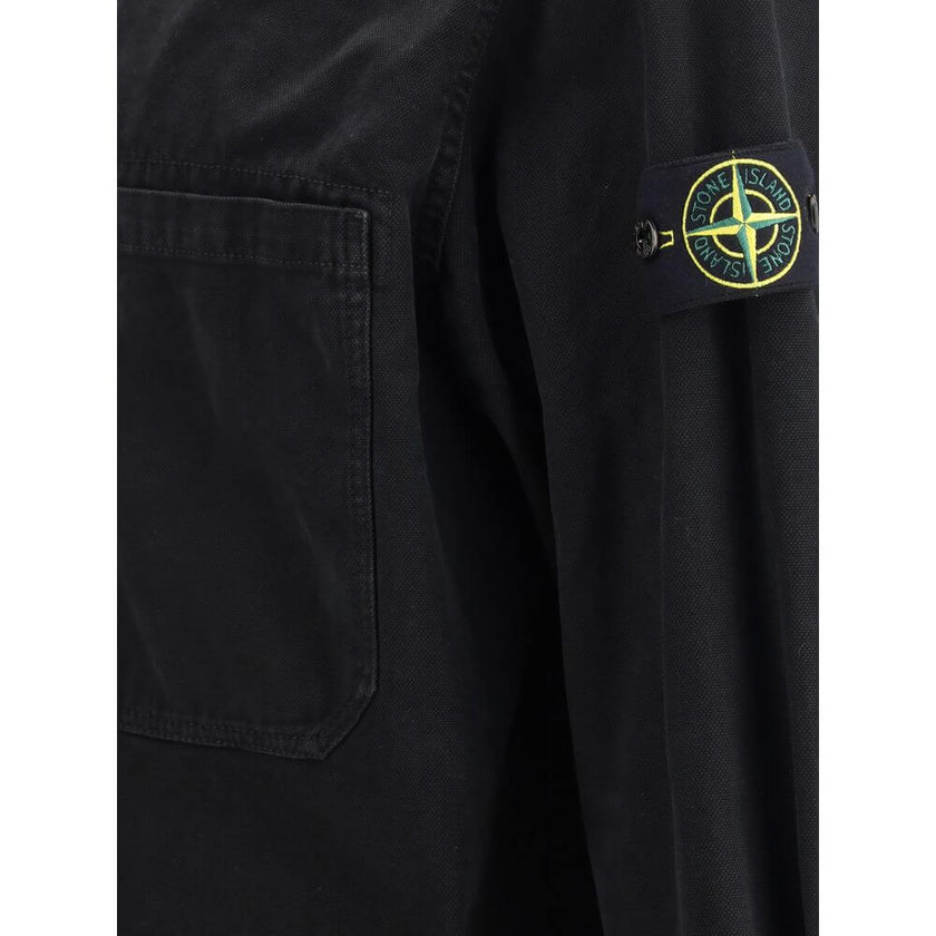 Black Cotton ShirtThe Stone Island Overshirt, crafted from 100% black cotton, is a versatile essential that blends functionality with contemporary style. Featuring a button fastening, two chest patch pockets, and the iconic logo patch on the left sleeve,